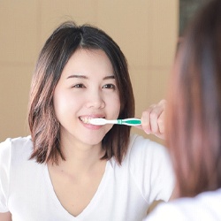 Woman brushing her teeth while looking into the mirror