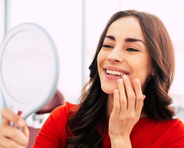 Woman looking at smile after dental implant tooth replacement