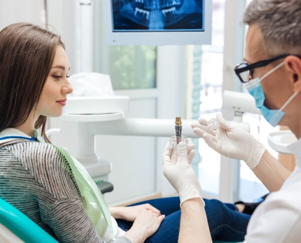 Dentist and patient looking at model dental implant post