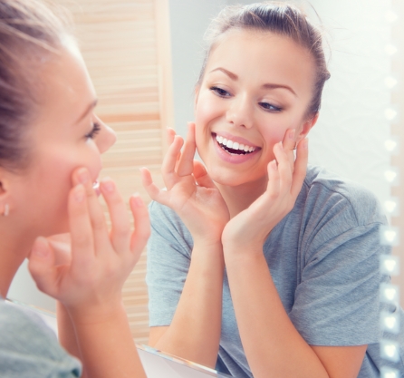 Smiling young woman looking at herself in the mirror and touching her face