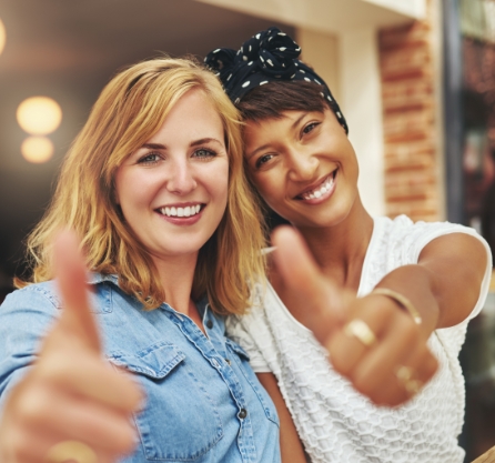 Two young women grinning and giving thumbs up