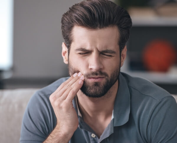 Man in need of wisdom tooth extraction holding cheek in pain