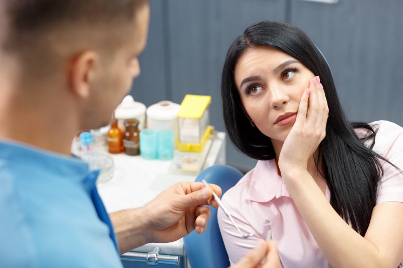 A woman holding her cheek due to wisdom tooth pain at the dentist